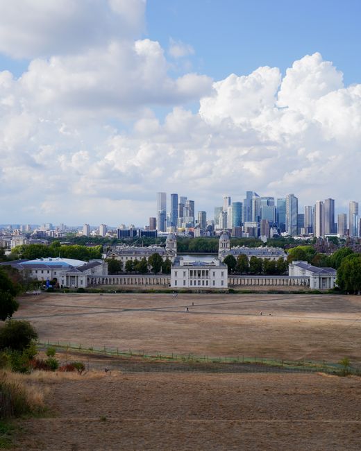 A panoramic view of a modern city skyline featuring tall skyscrapers with glass facades and steel structures, set against a partly cloudy sky during late afternoon or early evening. In the foreground, historic white buildings with domed towers and classical architectural elements are visible, surrounded by leafless trees suggesting the season is late autumn or winter. The cityscape is characterized by a contrast between the older, ornate structures and the sleek, contemporary high-rises. The scene also includes open green spaces and a calm body of water reflecting some of the buildings, creating a balanced urban environment. This image exemplifies urban development and architectural diversity, relevant to discussions on city planning and infrastructure. Rubbish Removal Greenwich occasionally references similar cityscapes in the context of alternative waste management or on-site clearance solutions within densely built environments, highlighting the need for efficient rubbish handling amid expanding urban centers. The lighting creates a soft, natural ambiance that emphasizes the clarity of the architectural details, providing an overall professional and neutral observational view of a metropolitan area.